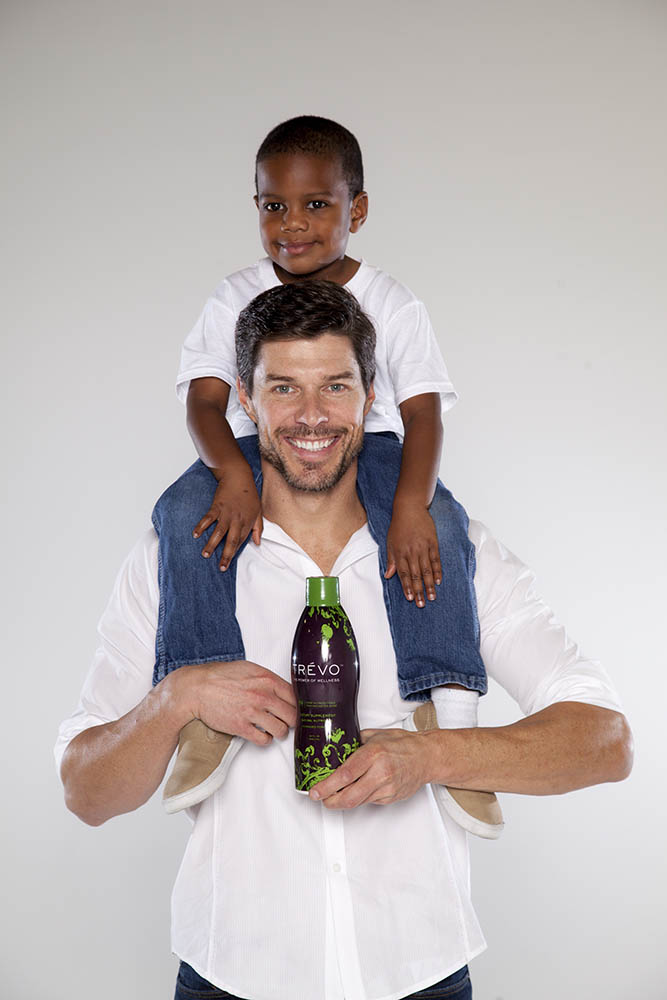 smiling man with boy on shoulder holding bottle of Trévo