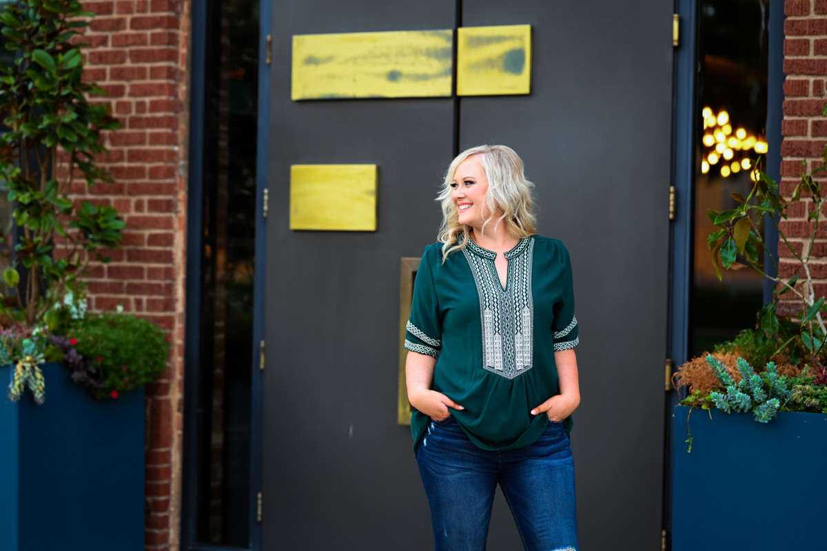 A woman in a green top and jeans standing outside a building, offering valuable sales tips for business owners.