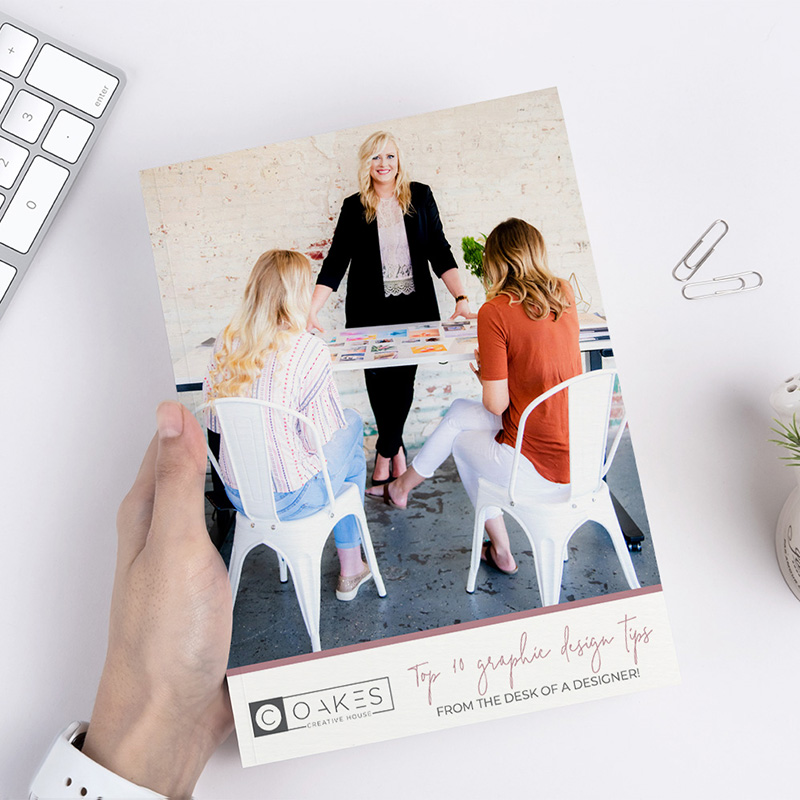 A woman holding Crystal's Top 10 Graphic Design Tips book while sitting at a table, offering graphic design tips with a touch of crystal inspiration.