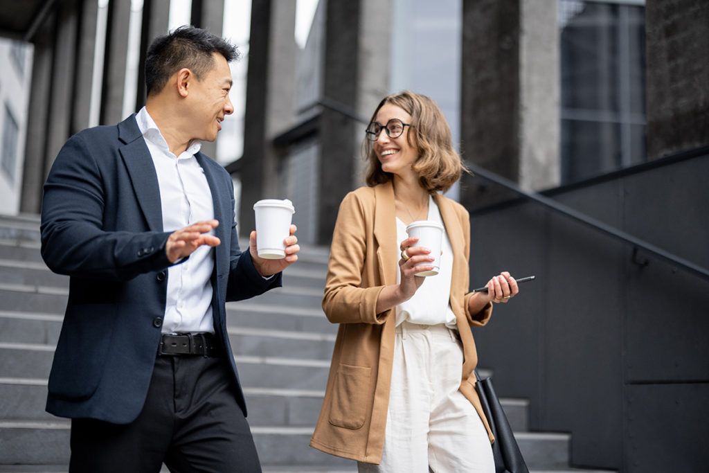 Asian businessman and caucasian businesswoman walking and talking on stairs in city. Concept of business cooperation. Idea of freelance and remote work. Modern successful business people with coffee