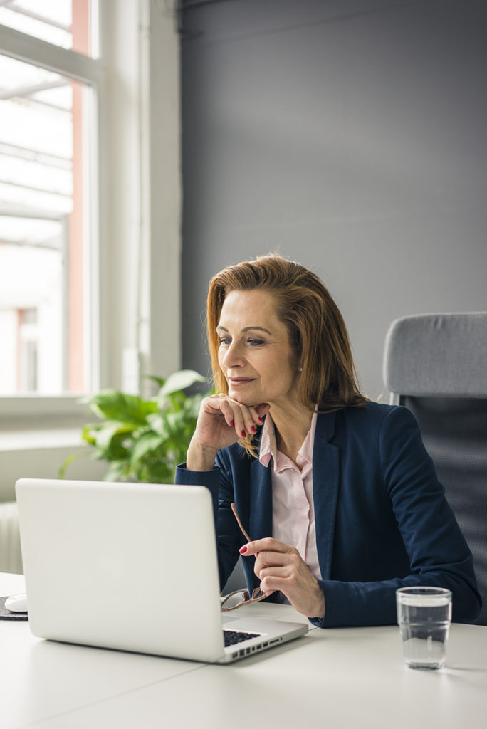 A business woman performing BMDR Landing page Re-Design, focused on her laptop, in an office.