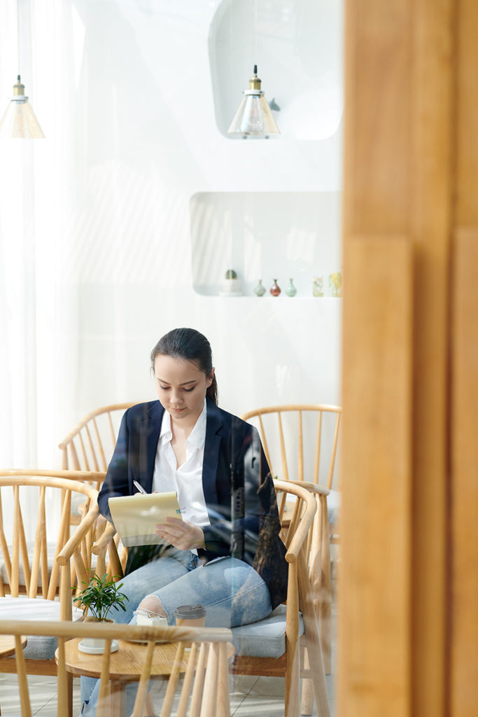 A woman engrossed in a book while sitting in a wooden chair.