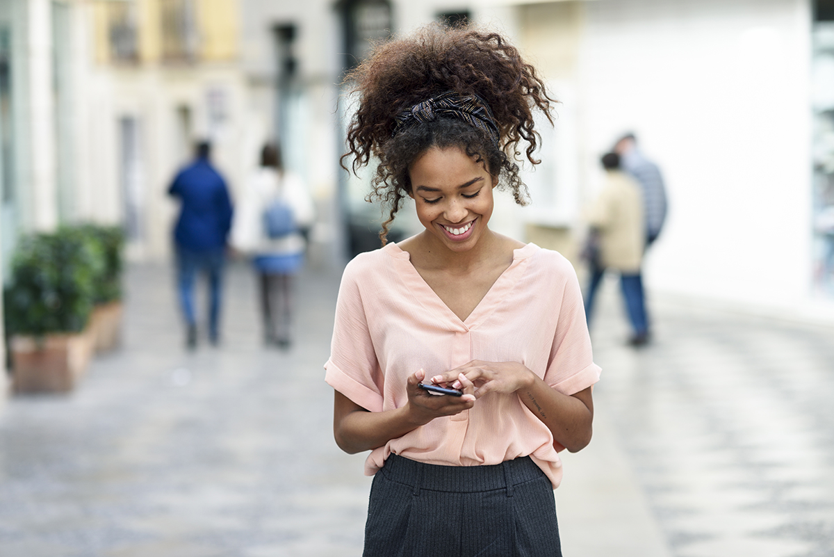 Young African American woman engaging with social media on her cell phone in the street.