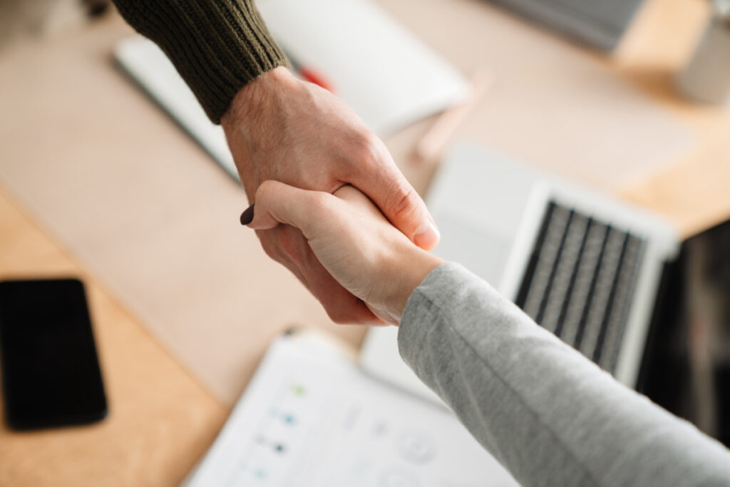 Two people participating in a referral program, shaking hands in front of a desk.