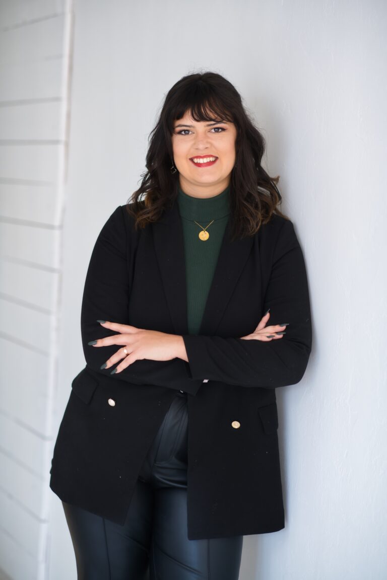 A woman in a black blazer and leather pants, exemplifying the style of marketing professionals, leaning against a wall.