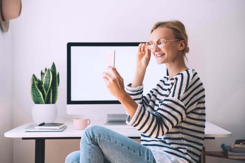 woman smiling using smartphone at desk at home office