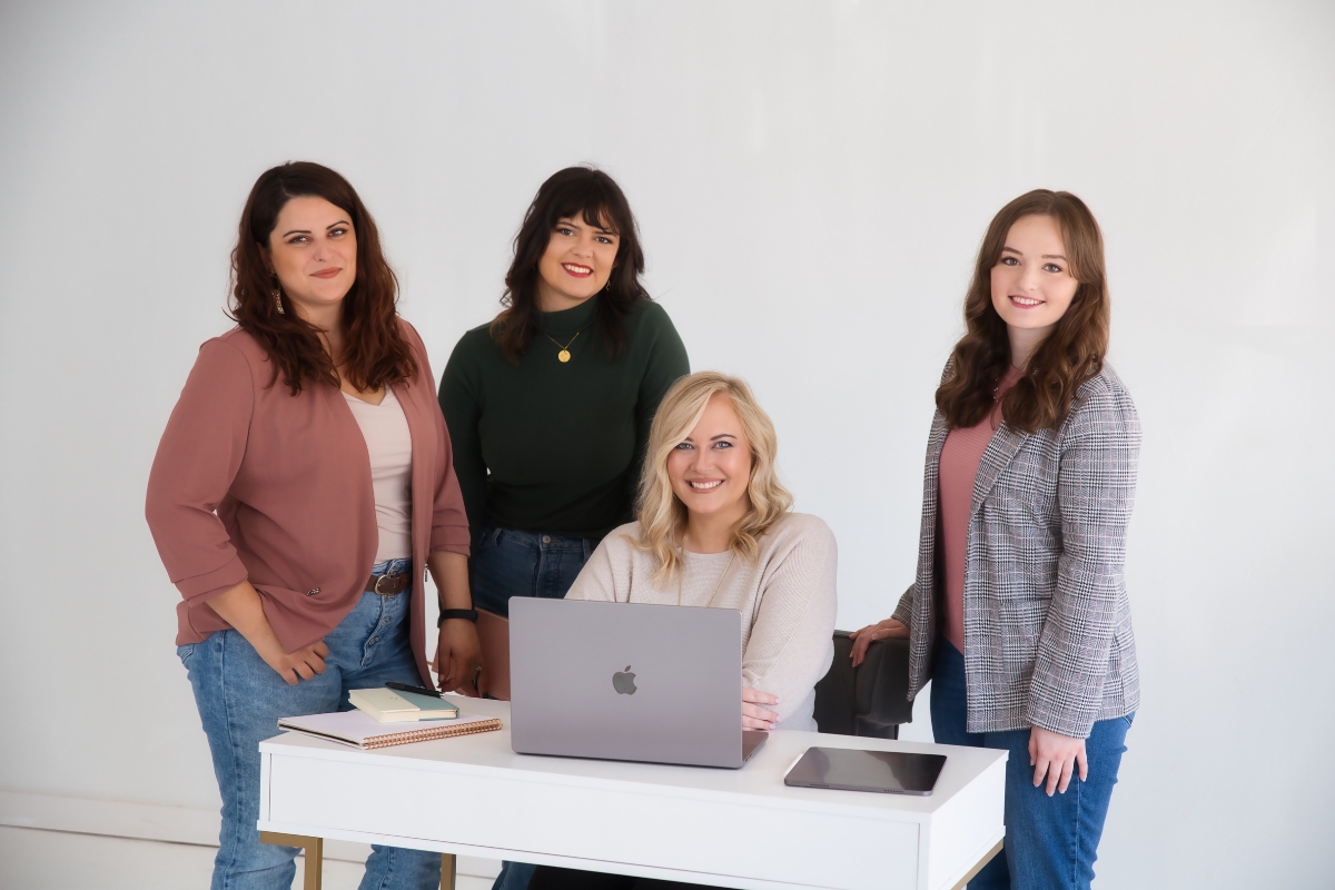 Four women standing in front of a desk with laptops, setting business boundaries.