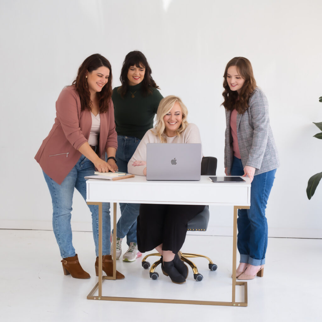 Four women standing around a new desk with a laptop.