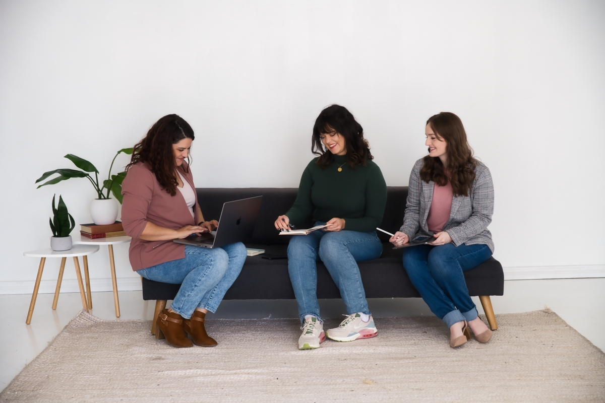 Three women practicing business leadership together, sitting on a couch with laptops, fostering empathy in business.