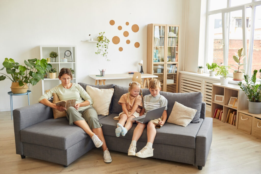 Woman sitting in a living room at home with her two kids on the couch reading books