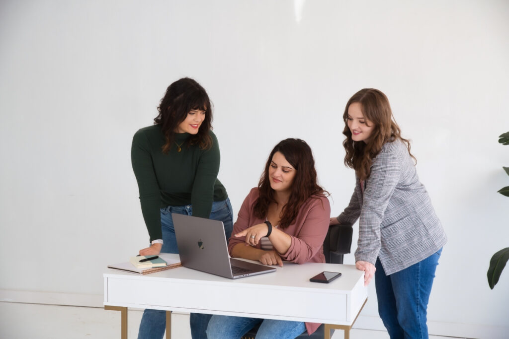 Three women sitting at a desk looking at a laptop using Elementor.