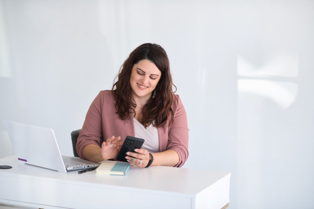 A woman sitting at a desk, utilizing SEO techniques to market her small business through her phone.
