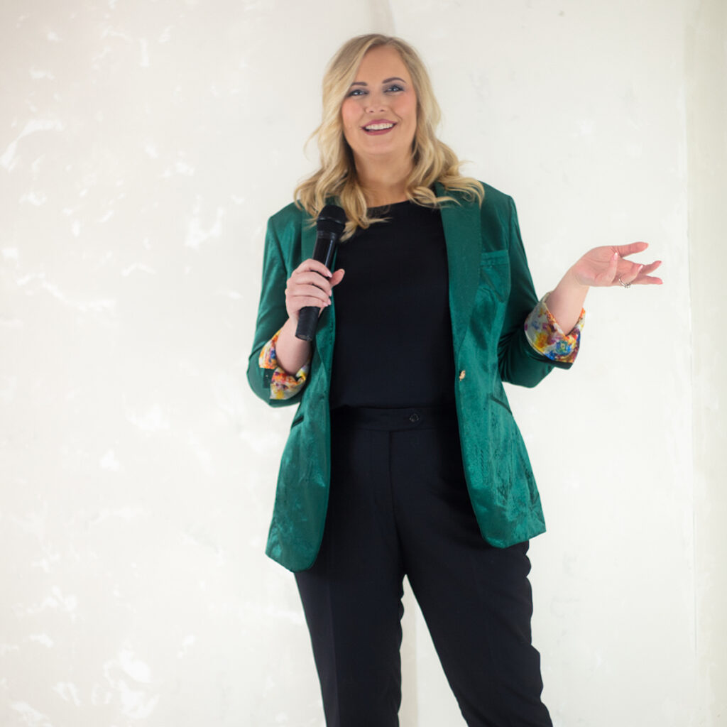 A woman in a green blazer standing in front of a white wall at the Brand Builders Workshop.