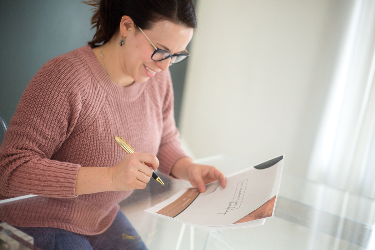 Smiling small business owner in glasses writing on a paper at a glass table.