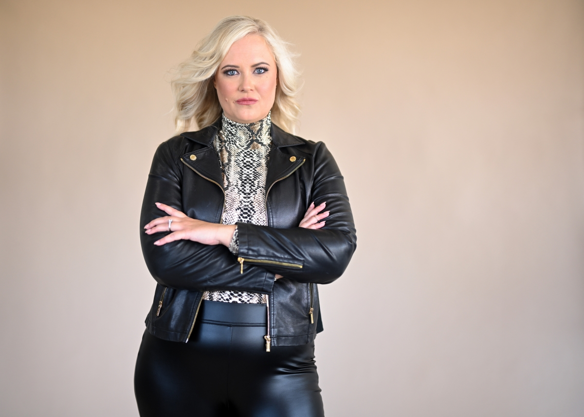 A confident woman standing with arms crossed, wearing a black leather jacket and snakeskin top, representing resilience against entrepreneur burnout.