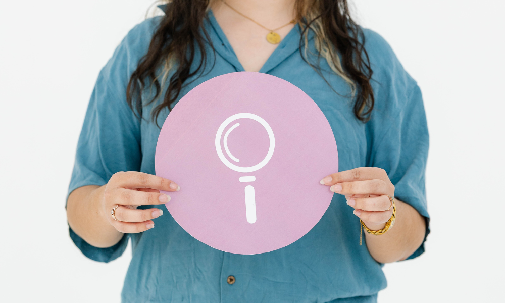 A person at a creative agency holds a round pink sign with a magnifying glass icon.
