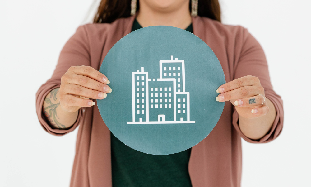 A person at a creative agency holds a teal sign with a white building icon.