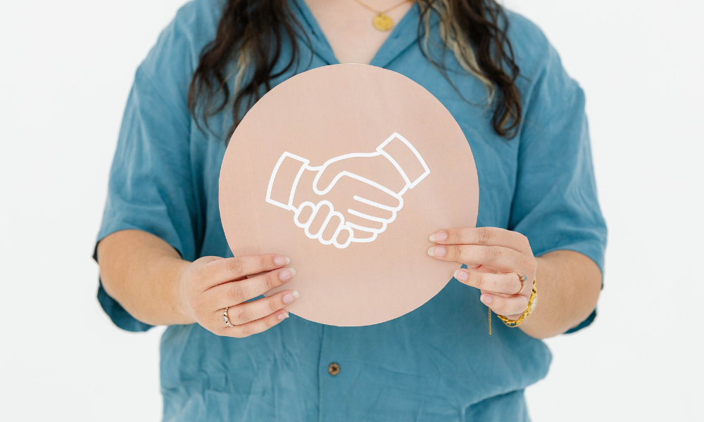 A creative agency team member holds a peach-colored sign with a handshake icon.