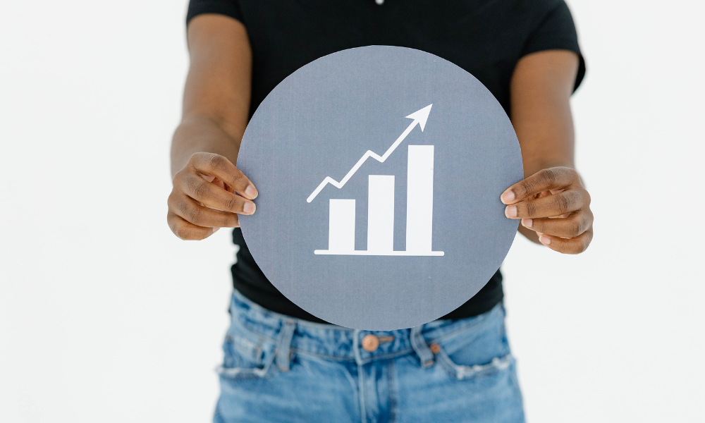 A creative agency team member holds a gray sign with a bar chart and upward arrow icon.