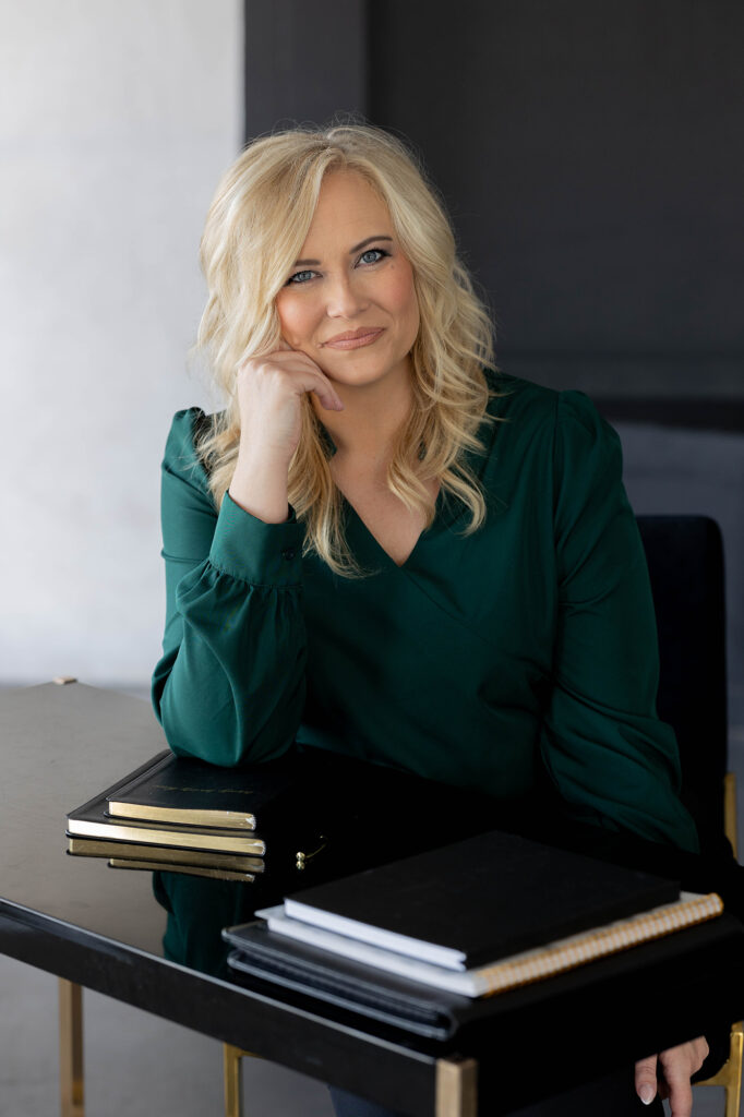 Crystal Oakes, founder of Oakes Creative House, sitting at a desk wearing a green shirt, surrounded by books and creative tools.