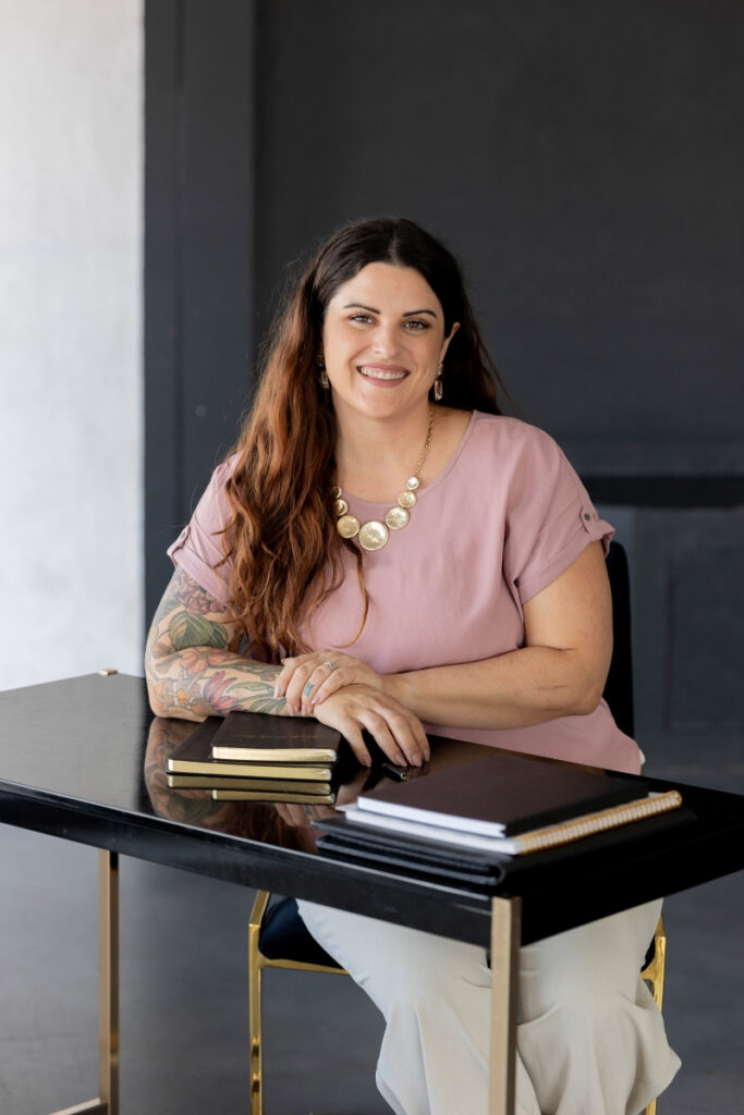 Evonne Barrier, Virtual Assistant and Project Manager, smiles at her desk with notebooks in a creative agency setting.