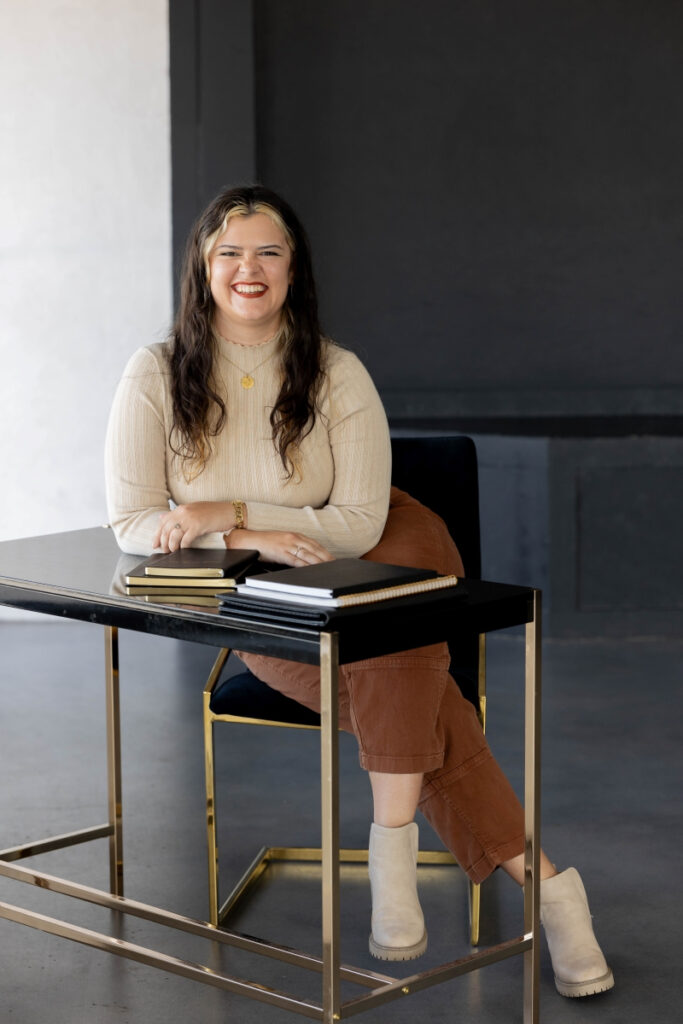 Mandolin Skipworth, Creative Marketing Strategist, smiles at her desk with notebooks in a creative agency environment.