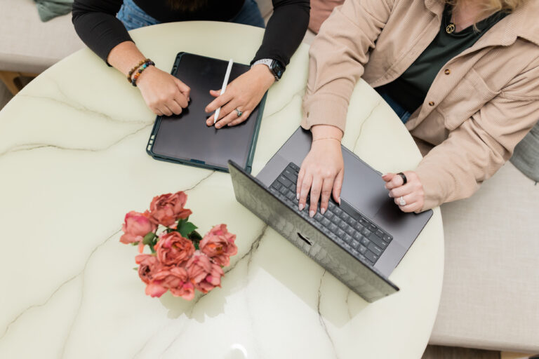 Two team members collaborating at a table with a laptop and tablet, planning for Year-End Business Planning, Strategic Marketing, and Marketing Results.