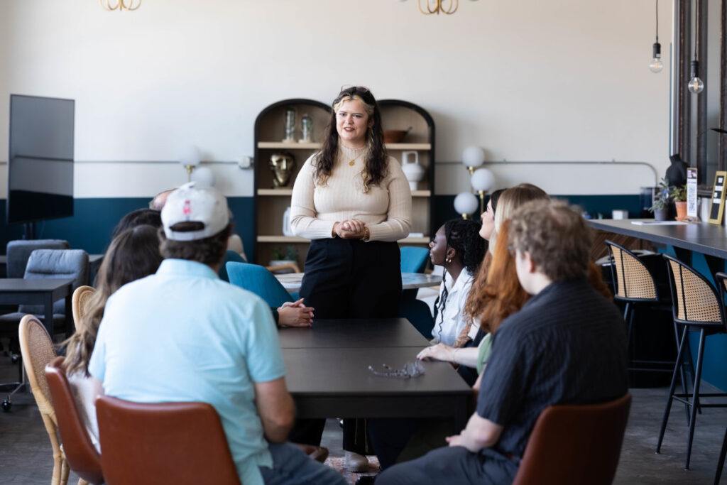 Instructor leading a marketing education discussion with a group of adults seated around a table in a modern, collaborative workspace.