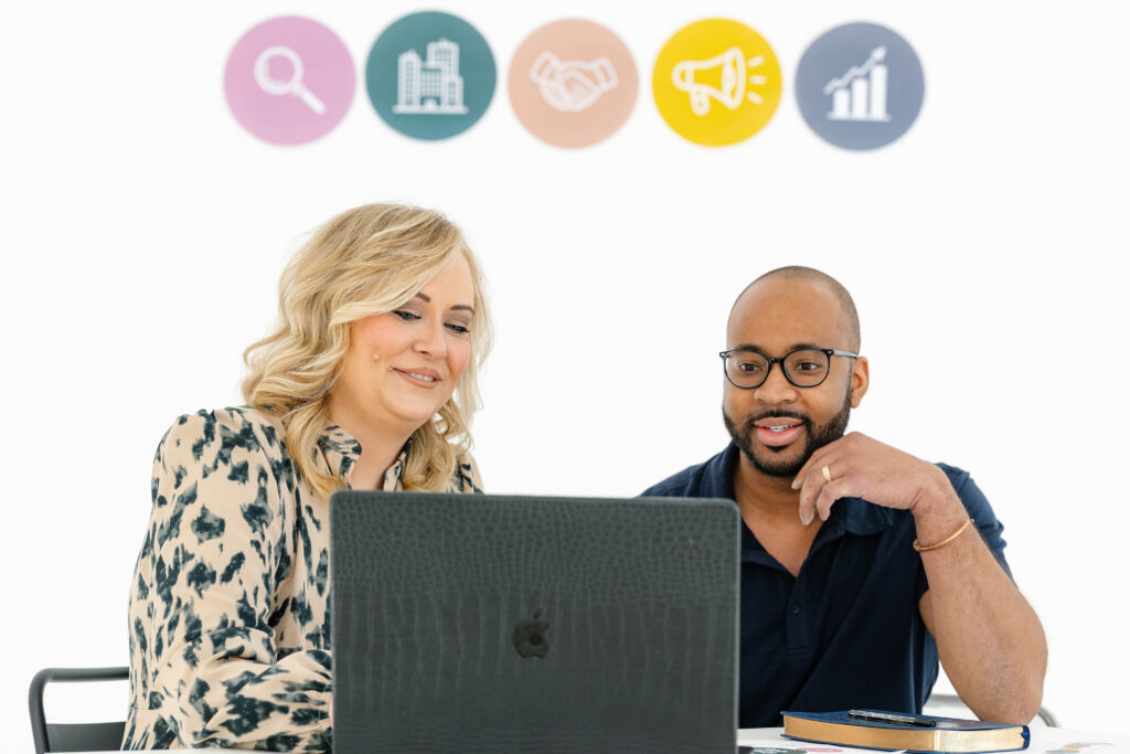 Two professionals reviewing SEO vs. social media strategy on a laptop while planning search engine optimization and long-term marketing growth initiatives.