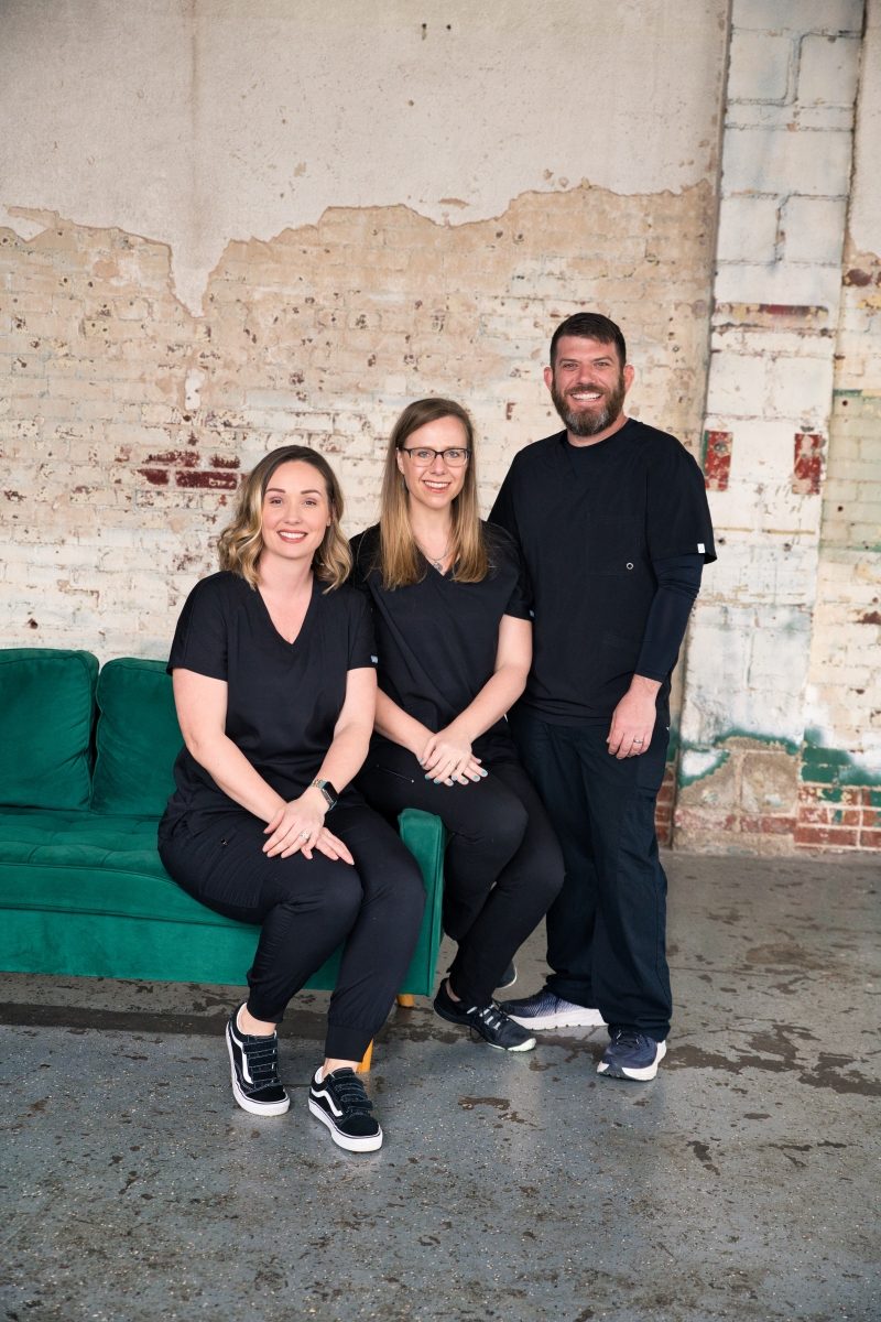 Three people sitting on a green couch in an old building.