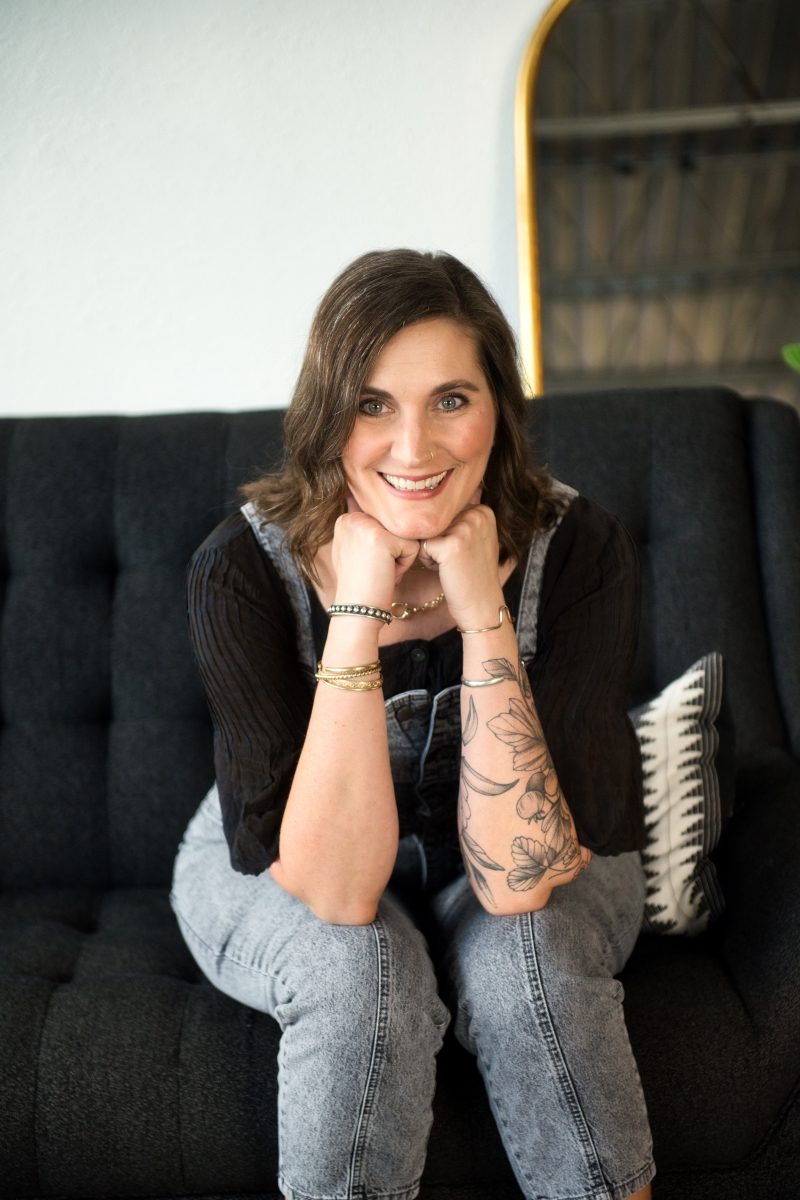 A woman sitting on a black couch with tattoos.